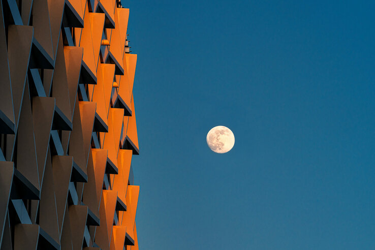 Modern building façade at sunset with a full moon in the clear sky.
