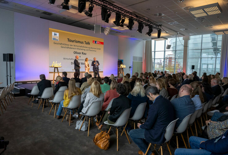 Vortrag im ATLANTIC Hotel Sail City, Bremerhaven: Drei Redner auf Bühne vor Publikum in modernem Konferenzraum.