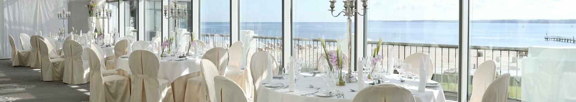 Bright dining room with set tables, chairs and sea views through large windows at the ATLANTIC Grand Hotel Travemünde.