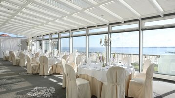 Veranstaltungsraum Baltic View im ATLANTIC Grand Hotel Travemünde Heller Speisesaal mit gedeckten Tischen, Stühlen und Meerblick durch große Fenster im ATLANTIC Grand Hotel Travemünde.