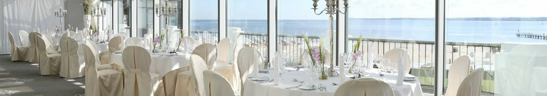 Veranstaltungsraum Baltic View im ATLANTIC Grand Hotel Travemünde Heller Speisesaal mit gedeckten Tischen, Stühlen und Meerblick durch große Fenster im ATLANTIC Grand Hotel Travemünde.