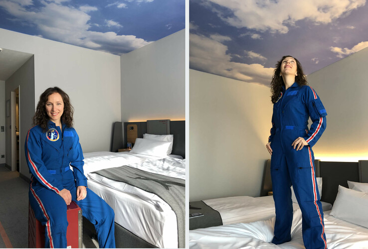 Frau in blauem Raumanzug in Hotelzimmer mit Wolkendecke und modernem Bett im ATLANTIC Hotel Airport Bremen.