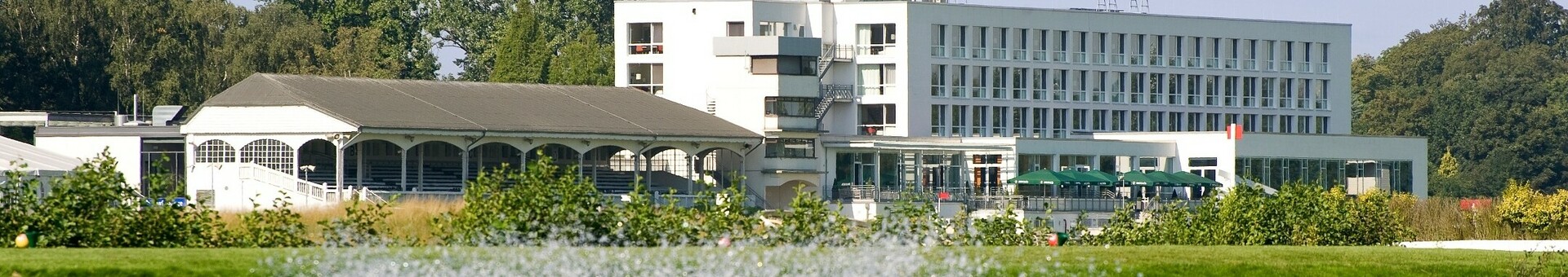 Wasserspiel auf dem See vor dem ATLANTIC Hotel Galopprennbahn in Bremen ATLANTIC Hotel Galopprennbahn in Bremen, modernes Gebäude am Wasser mit Springbrunnen im Vordergrund, umgeben von Natur.