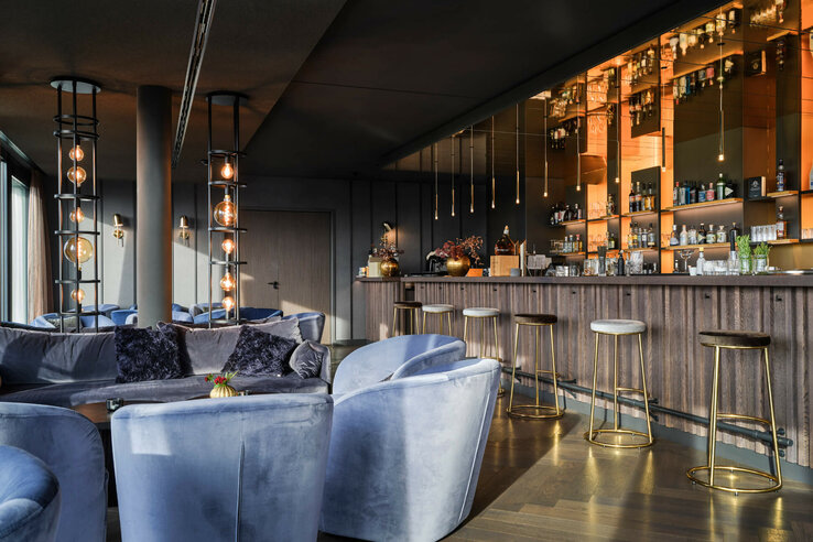 Modern hotel bar with blue velvet armchairs, elegant hanging lamps and a well-stocked bar at the ATLANTIC Hotel Münster.