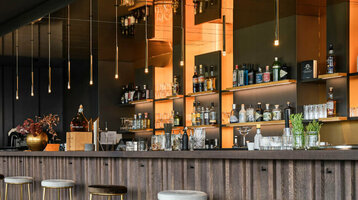 Moderne Hotelbar mit blauen Samtsesseln, eleganten Hängelampen und einer gut bestückten Theke im ATLANTIC Hotel Münster.