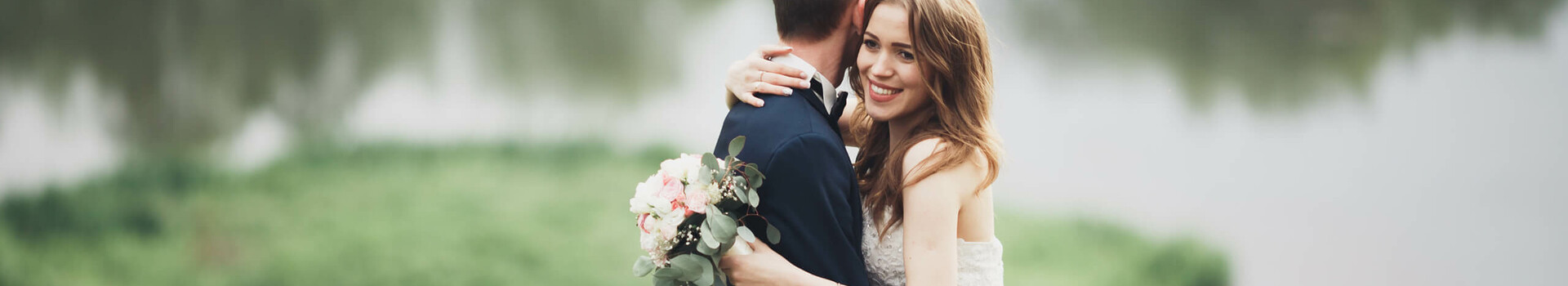 Hochzeit ATLANTIC Hotel Universum Ein Brautpaar umarmt sich vor einem See, die Braut hält einen Blumenstrauß.