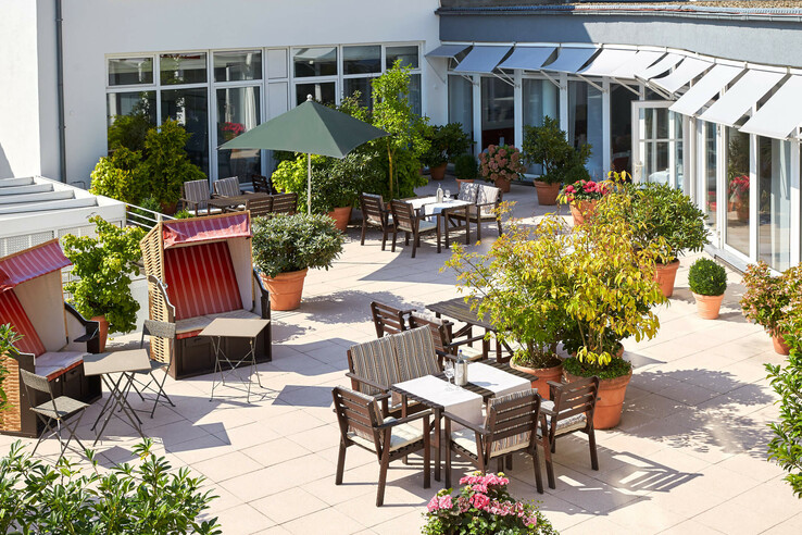 Sunny hotel terrace with beach chairs, tables and plants at the ATLANTIC Hotel Vegesack in Bremen.