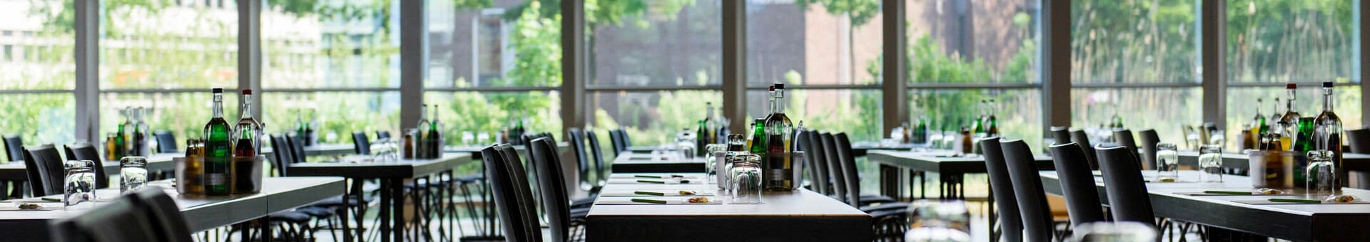 Veranstaltungsraum im ATLANTIC Hotel Universum Bremen Moderner, heller Konferenzraum mit langen Tischen, Stühlen und großen Fenstern mit Blick auf grüne Bäume.