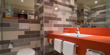 Modern bathroom with red washbasin, towels and shower at the ATLANTIC Hotel Galopprennbahn, Bremen.