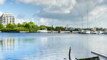 View of the ATLANTIC Hotel Wilhelmshaven on the waterfront with the marina and blue sky in the background.