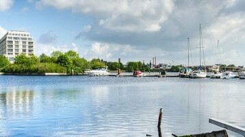 Blick auf das ATLANTIC Hotel Wilhelmshaven am Wasser mit Yachthafen und blauem Himmel im Hintergrund.