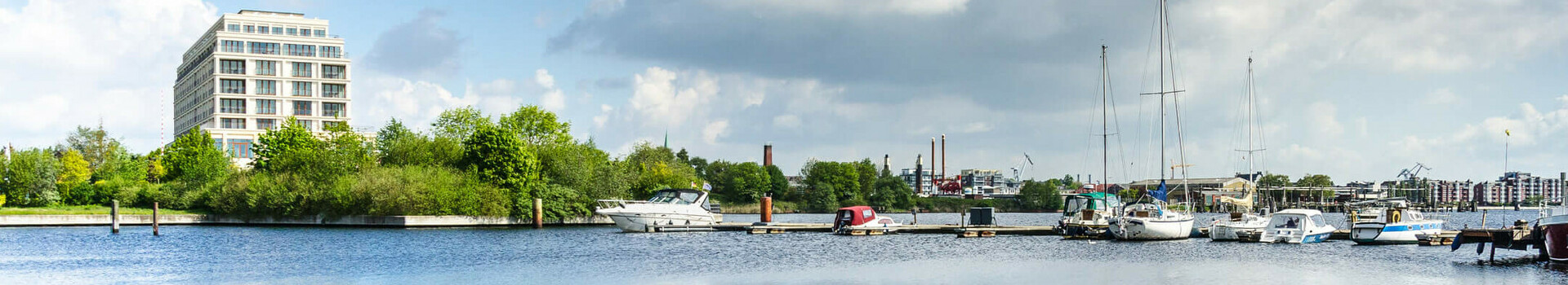 View of the ATLANTIC Hotel Wilhelmshaven on the waterfront with the marina and blue sky in the background.