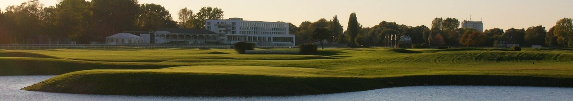 Green racecourse with pond, ATLANTIC Hotel in the background under a blue sky.