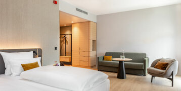 Modern hotel room with double bed, sofa, armchair and table, light colors, minimalist design at the ATLANTIC Hotel Heidelberg.