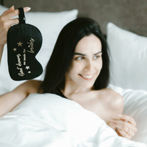 Sweet dreams vor dem großen Tag im ATLANTIC Grand Hotel Bremen Frau lächelt im Bett und hält eine Schlafmaske mit der Aufschrift "Sweet dreams are made for brides".
