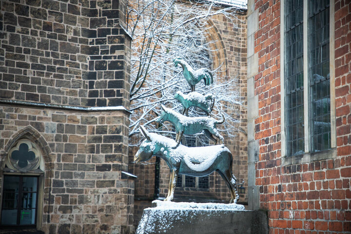 Schneebedeckte Bremer Stadtmusikanten-Statue vor historischer Backsteinfassade im Winter.