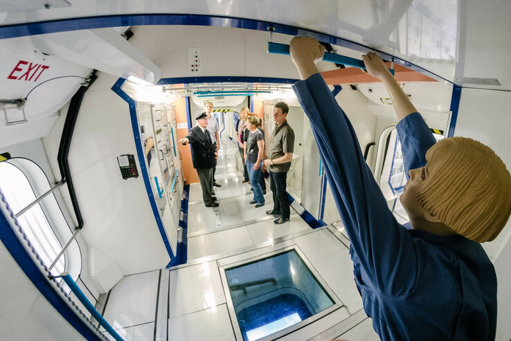 Personengruppe in einem Raumstationsnachbau, umgeben von technischen Geräten und einer Schaufensterpuppe im Vordergrund.