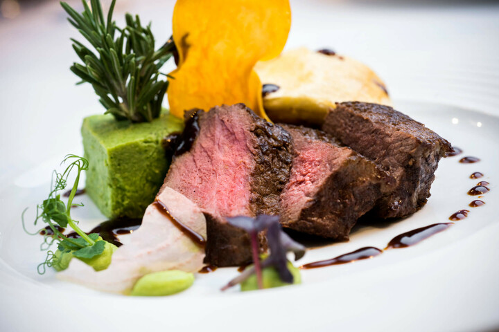 Speisen und Getränke im ATLANTIC Grand Hotel Travemünde Gourmetgericht mit saftigem Rindfleisch, grünem Püree und dekorativem Rosmarinzweig auf elegantem Teller.