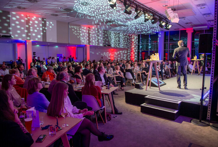 Ein Redner auf einer Bühne vor einem vollen Publikum in einem modern beleuchteten Konferenzraum des ATLANTIC Hotel Sail City.