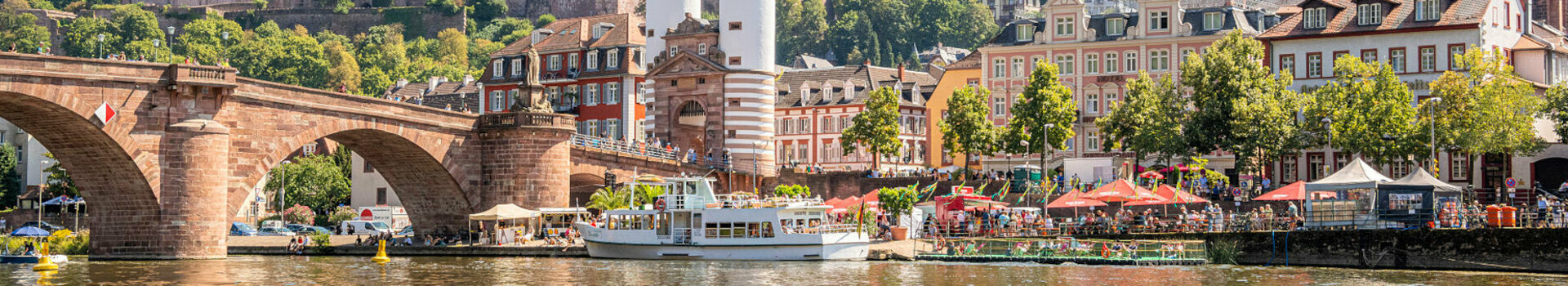 Historic old town by the river with bridge, castle and green hills in the background.