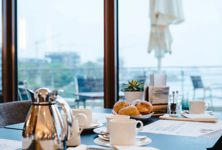 Set breakfast table with coffee pot, cups and rolls in a modern restaurant with a view of the terrace and city.
