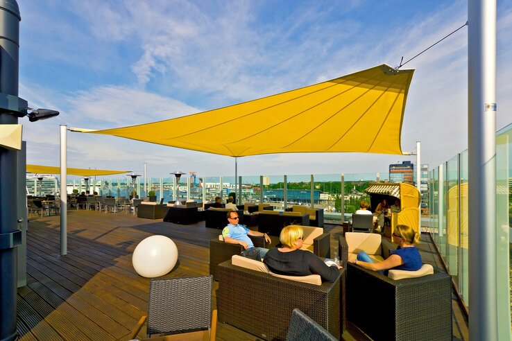 Hotel-Dachterrasse mit gelben Sonnensegeln, modernen Sitzmöbeln und Blick auf die Stadt Kiel.