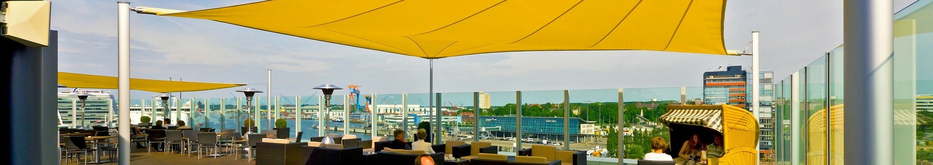Hotel-Dachterrasse mit gelben Sonnensegeln, modernen Sitzmöbeln und Blick auf die Stadt Kiel.