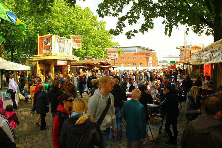 Lively market in Vegesack with people and food stalls under green trees.
