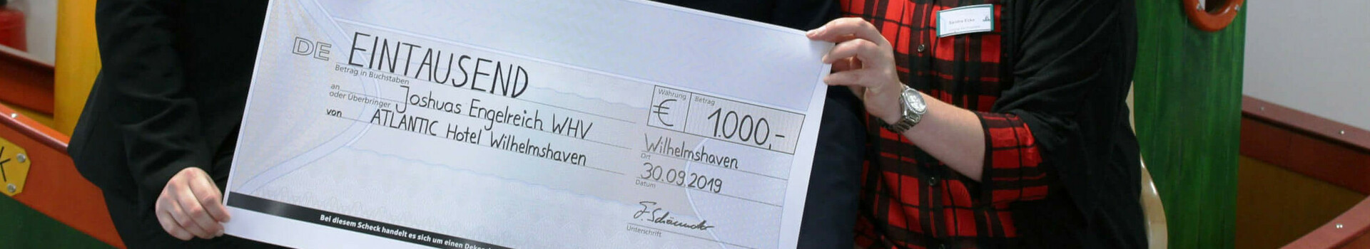Three people holding a large check for 1000 euros at the ATLANTIC Hotel Wilhelmshaven.