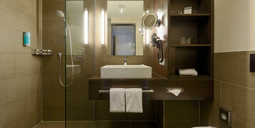 Modernes Hotelbad mit Glasdusche, Waschbecken, beleuchtetem Spiegel und Handtüchern im ATLANTIC Hotel Lübeck.