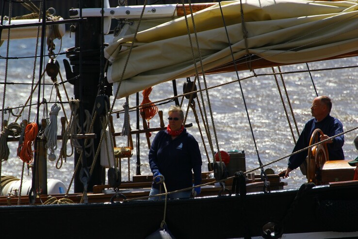 Two people on a sailing boat in sunny weather, surrounded by sails and ropes, on sparkling water.