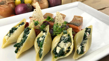 Gefüllte Muschelnudeln mit Spinat und Käse, garniert mit Lachs und Kräutern auf einem weißen Teller.