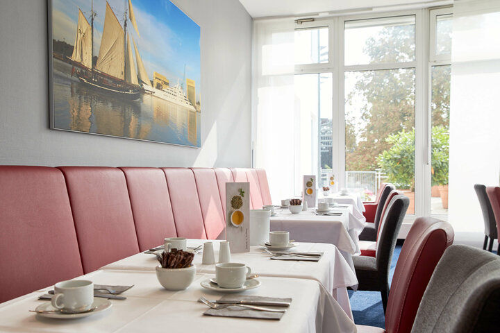Frühstücksraum im ATLANTIC Hotel Vegesack Heller Frühstücksraum mit gedeckten Tischen, roten Sitzbänken und großem Fenster im ATLANTIC Hotel Vegesack.