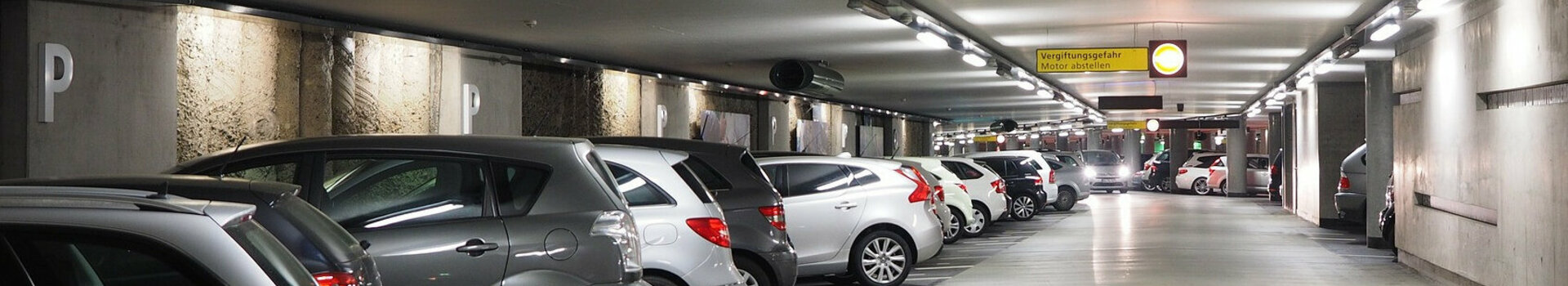 Bright underground parking garage with parked cars and signposts to the Rathaus/Münsterplatz exit at the ATLANTIC Grand Hotel Bremen.