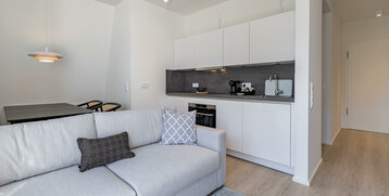Modern hotel suite with bright kitchen, gray sofa, dining table and stylish lighting.