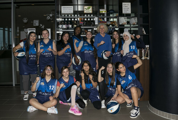 Youth basketball team poses in blue jerseys with basketballs at the ATLANTIC Hotel Sail City, Bremerhaven.