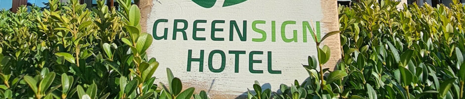 Hotelschild „Greensign Hotel“ umgeben von grünen Sträuchern.