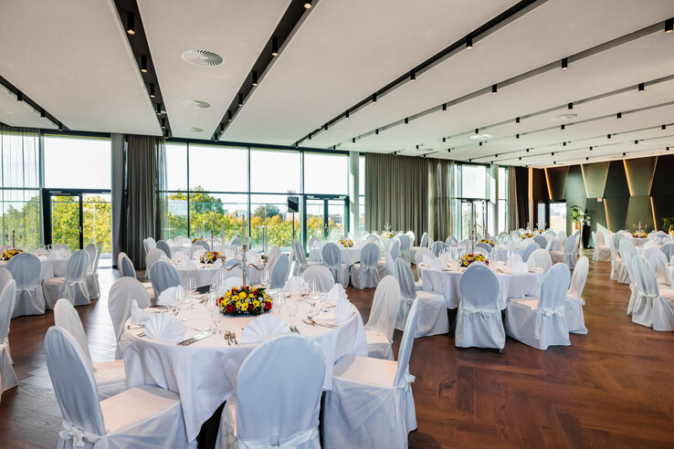 Elegant banquet hall in the ATLANTIC Hotel Münster with round, white-clothed tables and large windows.