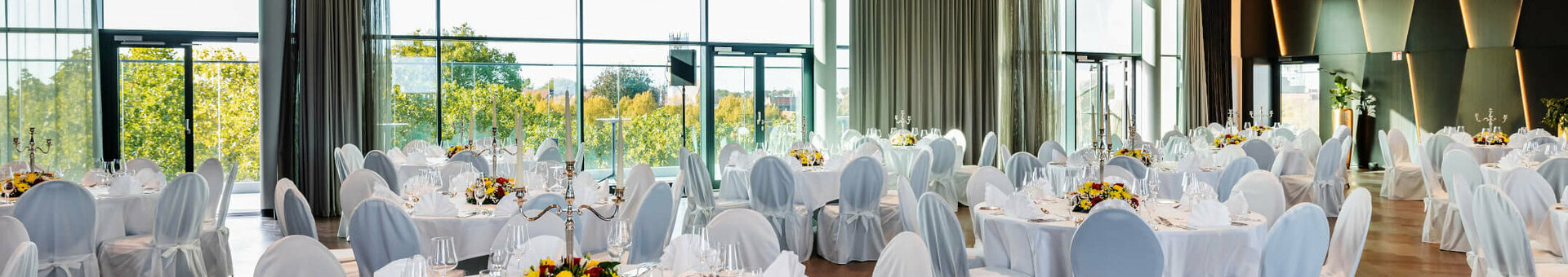 Engelsaal  Eleganter Bankettsaal im ATLANTIC Hotel Münster mit runden, weiß gedeckten Tischen und großen Fenstern.