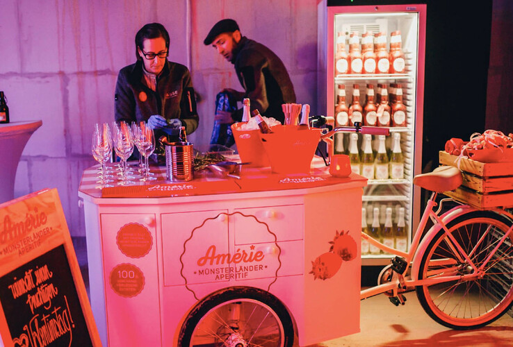 Bar mit Getränken und Gläsern, Fahrrad-Dekoration, Kühlschrank mit Flaschen, stimmungsvolle Beleuchtung im ATLANTIC Hotel Münster.