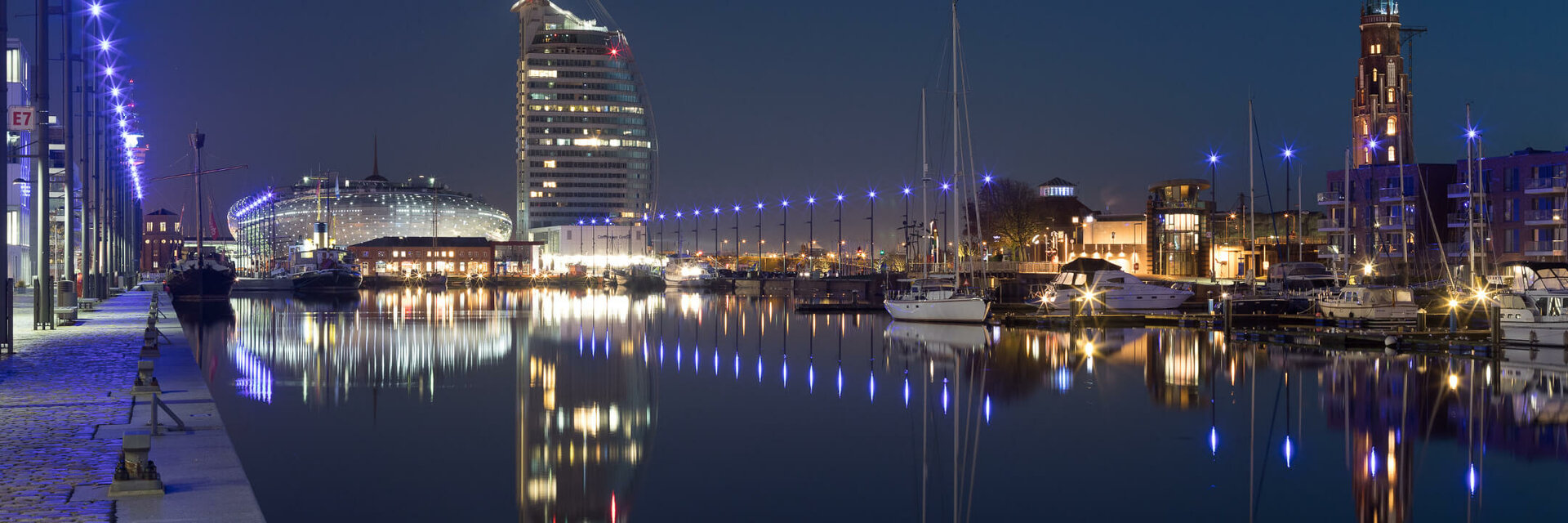 Night view of the ATLANTIC Hotel Sail City at the illuminated harbor of Bremerhaven with reflecting water.