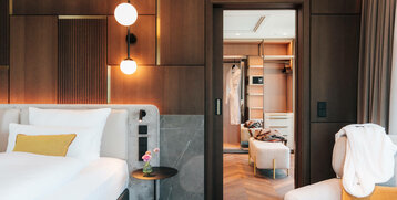 Modernes Hotelzimmer mit Doppelbett, stilvollen Holzwänden, beleuchtetem Nachttisch und offenem Kleiderschrank im ATLANTIC Hotel.