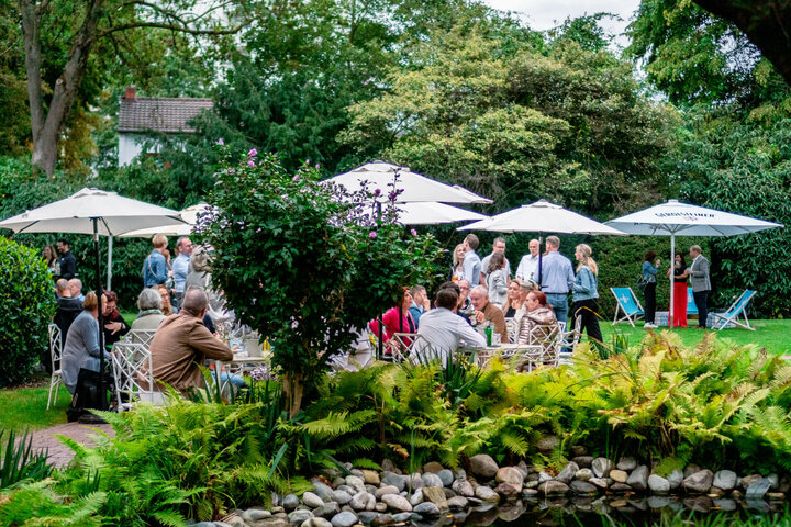 Garden area of the ATLANTIC Hotel with guests under parasols, surrounded by lush greenery and a small pond.