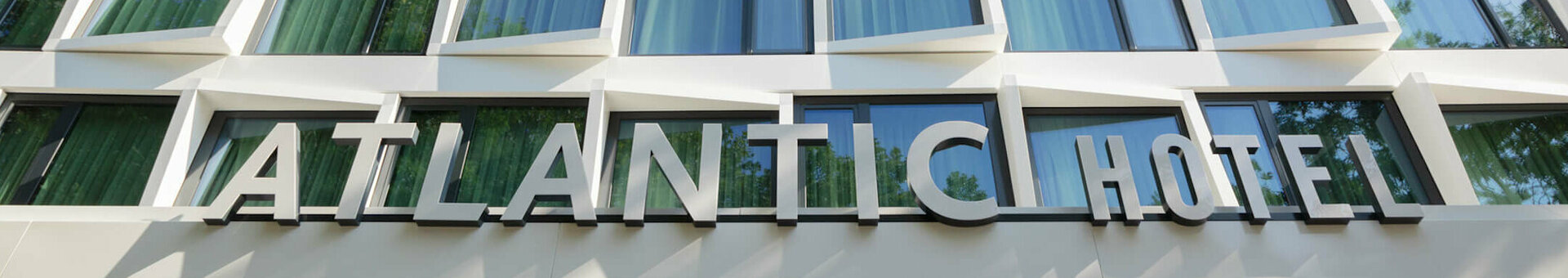 Modern façade of the ATLANTIC Hotel Münster with geometric windows and a green tree in the foreground.