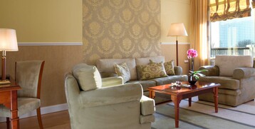 Elegantes Hotelzimmer mit beigen Sofas, Holztisch, Orchidee, gemusterter Tapete und großen Fenstern mit Vorhängen.