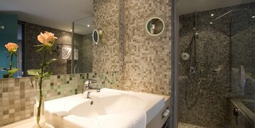 Modern bathroom in the ATLANTIC Hotel Universum with mosaic tiles, washbasin, shower and decoration with roses.