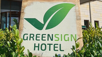 Facade of a modern hotel with "Greensign Hotel" sign and green plants in the foreground.