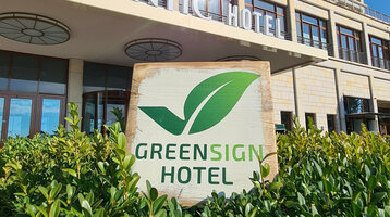 Fassade eines modernen Hotels mit "Greensign Hotel"-Schild und grünen Pflanzen im Vordergrund.