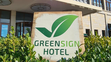 Facade of a modern hotel with "Greensign Hotel" sign and green plants in the foreground.