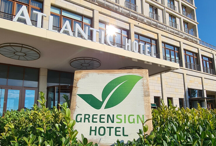 Facade of a modern hotel with "Greensign Hotel" sign and green plants in the foreground.